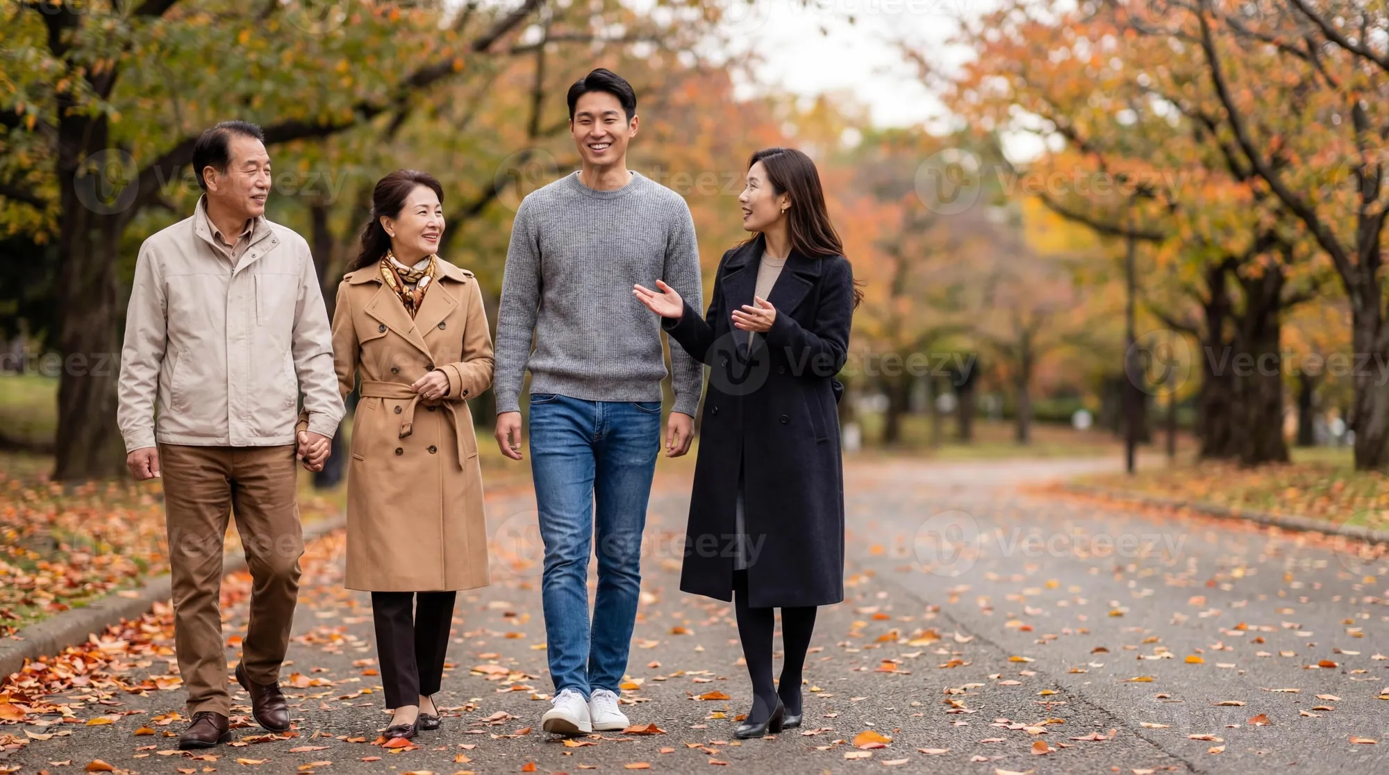 An adult son and daughter walking with their senior parents through a park in autumn